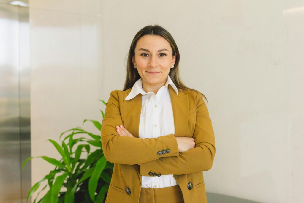 Confident woman in business suit standing indoors with crossed arms, smiling.